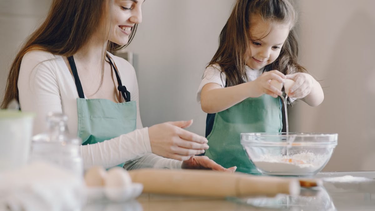 A joyful mother and daughter bond by baking together in a bright kitchen.